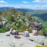 Hikers resting on large granite rocks at Old Rag mountain summit with forested valleys and blue sky in the background at Shenandoah national Park.