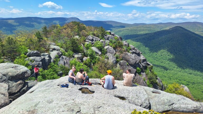 Hikers resting on large granite rocks at Old Rag mountain summit with forested valleys and blue sky in the background at Shenandoah national Park.